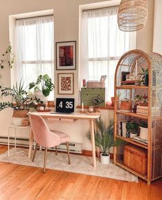 a home office with plants and pictures on the wall, including a pink chair in front of a desk