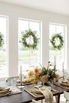 a dining room table is set with place settings and wreaths on the windowsill