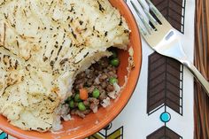 an orange bowl filled with mashed potatoes and peas next to a knife and fork