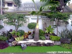 a garden with plants and rocks in front of a white building that says earth garden