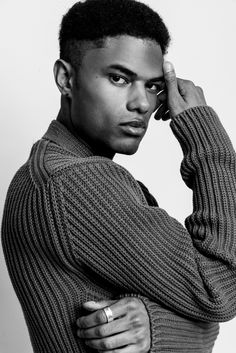 a black and white photo of a man in a sweater holding his hand to his head