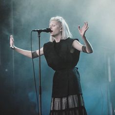 a woman standing in front of a microphone with her hands out to the side while singing