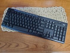 a black keyboard sitting on top of a wooden table next to a white doily