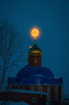 a building with a cross on top and the moon in the sky above it at night