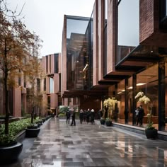 people are walking down the sidewalk in front of some tall buildings with plants and trees