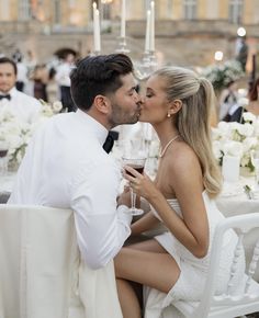 a man and woman kissing each other while sitting at a table with wine glasses in front of them