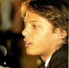 a young man wearing a suit and tie speaking into a microphone