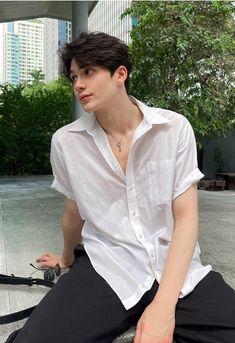 a young man sitting on the ground wearing a white shirt and black pants