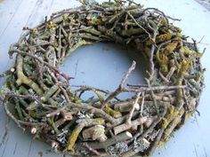 a wreath made out of branches and moss on a table top with a blue background