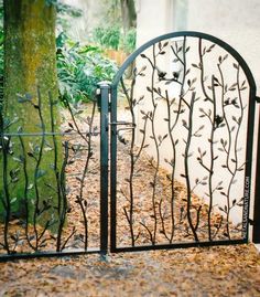 an iron gate in front of a white building with trees and bushes around it,