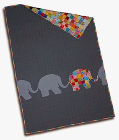 an elephant quilted on top of a gray blanket with multi - colored squares in the shape of elephants