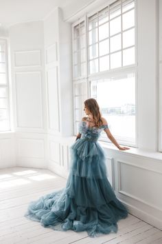 a woman in a blue dress leaning against a window