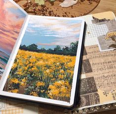 an open book sitting on top of a wooden table next to a painting and papers