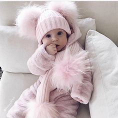 a baby in a pink outfit laying on top of a white couch next to pillows