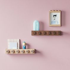 two wooden shelves with legos on them against a pink wall, one has a blue vase and the other is a framed photo