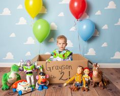 a little boy sitting in a box surrounded by toy figures and balloons with a sign that says grason is 2