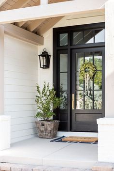 two potted plants are sitting on the front porch next to a black double door