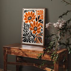 an orange and black flower art piece on a table next to a vase with flowers