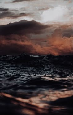 the sky is filled with dark clouds as it sits above the ocean waves in front of an orange and black sunset