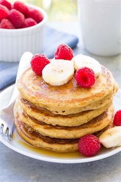 stack of pancakes with bananas and raspberries on the side, ready to be eaten