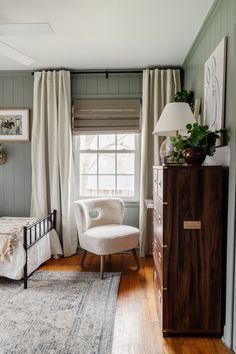 a bed room with a neatly made bed next to a window and a white chair