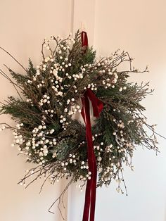 a wreath with white flowers and red ribbon hanging on a door handle in front of a wall