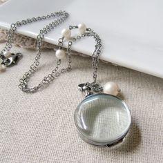 "This beautiful silver and glass locket has an heirloom feel. The round locket is double sided and has a swivel bail so the contents can be seen from either side. The translucent pale green glass is encased with sterling silver and domed to highlight the treasure beneath. There is room enough for two photos or a locket of hair. The locket opens and closes securely by twisting the silver bead \"nut\" at the top. The stylish locket is suspended from an oxidized sterling silver chain accented with Elegant Handmade Metal Locket Necklace, Elegant Round Metal Locket Necklace, Elegant Nickel-free Round Pendant Locket Necklace, Nickel-free Round Glass Jewelry, Vintage Charm Locket Necklace, Silver Glass Necklace Keepsake, Silver Round Locket Necklace With Lobster Clasp, Elegant Handmade Round Pendant Locket Necklace, Silver Glass Jewelry For Keepsake