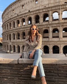 a woman sitting on top of a stone wall next to an old roman collise