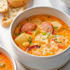 there is a bowl of soup with sausage and potatoes in it next to two slices of bread