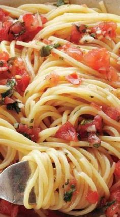 a close up of a plate of pasta with tomatoes and herbs on top, with a spoon in it