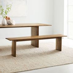 a wooden table with two benches in front of it and a vase on the floor