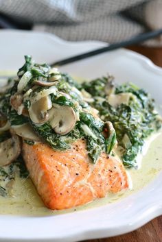 a white plate topped with salmon, mushrooms and spinach