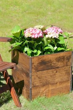 a wooden planter with flowers in it next to a chair on the grass outside