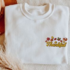 "🍂🧡 Dive into the heart of autumn with our \"Thankful\" Embroidered Thanksgiving Sweatshirt, capturing the essence of gratitude and the beauty of the fall season! Elevate your festive style with this uniquely crafted Thanksgiving Shirt. At its center, the word \"Thankful\" is embroidered in a heartwarming font, surrounded by intricate fall leaves and delightful autumnal graphics. It's more than just a statement; it's a sentiment, making this Thanksgiving Sweater a must-have for anyone wishing to express their gratitude in style. Whether you're gathering around a dinner table or exploring a pumpkin patch, this Fall Sweatshirt is your perfect companion. Its versatile design makes it a seamless fit for both a Thanksgiving feast and a Halloween adventure. Speaking of pumpkins, the subtle Emb White Embroidered T-shirt For Fall, White T-shirt With Embroidered Text For Fall, Custom Embroidery Long Sleeve T-shirt For Fall, White T-shirt With Custom Embroidery For Fall, Custom Embroidered White T-shirt For Fall, White Custom Embroidered T-shirt For Fall, White Embroidered Text T-shirt For Fall, White Embroidered Sweatshirt For Fall, Embroidered White T-shirt For Fall