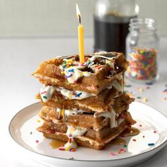 a stack of waffles topped with frosting and sprinkles next to a candle