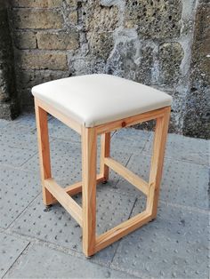 a wooden stool sitting on top of a stone floor next to a brick wall in front of a building