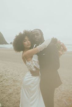 a bride and groom pose for a photo on the beach