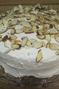 a cake with white frosting and almonds on top sitting on a glass plate