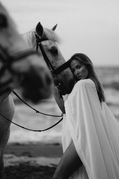 a woman standing next to a horse on the beach with her head resting on it's bridle