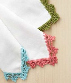 three pieces of white and green crocheted cloth on a wooden table with wood background