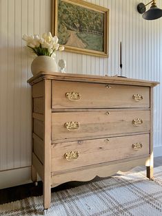 an old dresser with flowers in a vase on top and a painting hanging above it