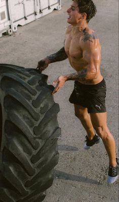 a shirtless man holding onto a large tire