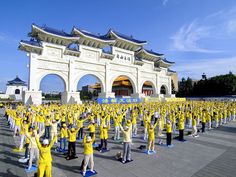 a large group of people standing in front of a white building with yellow shirts on