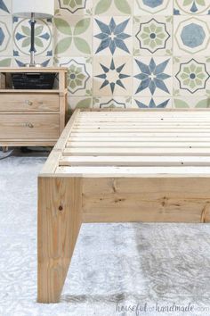 a wooden bed frame sitting in front of a wall with blue and green tiles on it