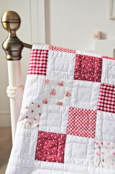 a red and white quilt sitting on top of a bed next to a wooden post