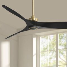 a ceiling fan in a living room with white walls and windows behind it is a gold light fixture