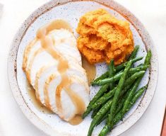 a white plate topped with green beans and chicken covered in gravy next to mashed potatoes