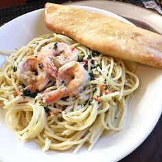 a white plate topped with pasta and shrimp next to a piece of bread on top of a table