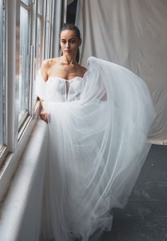 a woman in a white dress standing by a window