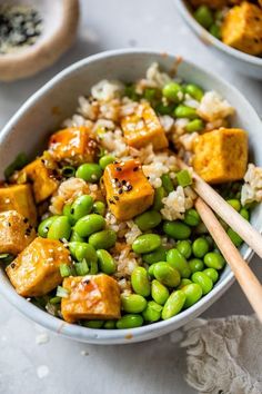 two bowls filled with rice, peas and tofu next to wooden chopsticks